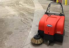 A walk-behind floor sweeper next to a clean streak on a cement floor.